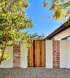 a wooden gate in front of a white wall and some green leaves on the ground