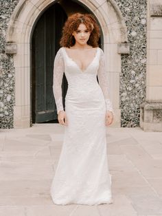 a woman standing in front of a building wearing a white wedding dress with long sleeves