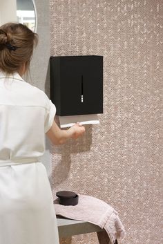 a woman in a white dress is holding up a black square device on the wall