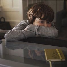 a young boy sitting at a table with his hands on his face and looking off into the distance