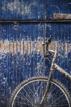 an old bicycle is parked in front of a rusty blue door with peeling paint on it