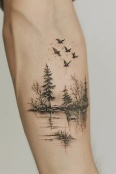 a person with a tattoo on their arm that has birds flying over water and trees