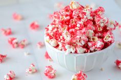 a white bowl filled with red and white popcorn on top of a table next to scattered candy