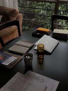 a table with books, coffee cup and laptop on it in front of a window