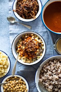 several bowls of food on a table with spoons and utensils next to them