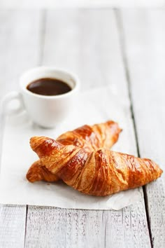 two croissants sitting next to a cup of coffee