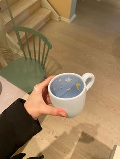 a person holding a coffee cup in their hand with the moon and stars painted on it