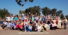 a group of people standing next to each other in front of a tree with their hands up