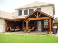 a covered patio with chairs and grill in the back yard, next to a large house