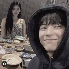 two people sitting at a table with food on it and one person wearing a hoodie