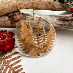 a glass ornament with gold leaves and a red flower next to it on a branch