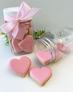 pink heart shaped cookies in a jar next to two hearts and a bow on the lid