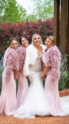 three bridesmaids in pink dresses and fur stoles posing for a photo together