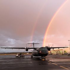 an airplane on the tarmac with a rainbow in the sky and two planes parked nearby