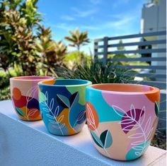 three colorful flower pots sitting on top of a white ledge