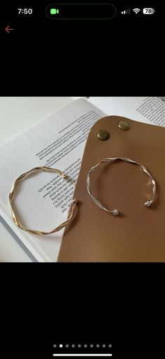 a pair of gold bracelets sitting on top of an open book next to a cell phone