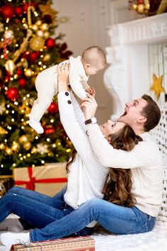 a man and woman holding a baby in front of a christmas tree