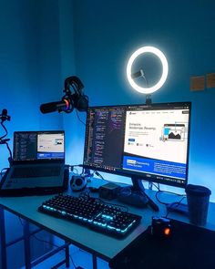 a desk with two laptops and a computer monitor on it in front of a blue light