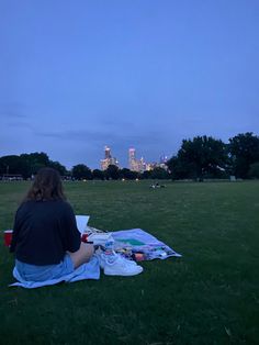 a woman sitting on top of a blanket in a field next to a city skyline