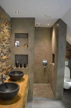 two black bowls are on the counter in this modern bathroom with stone walls and flooring