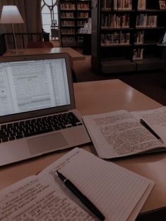 an open laptop computer sitting on top of a wooden desk next to two notebooks