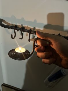 a hand holding an umbrella hook with a lit candle in front of it on a wall