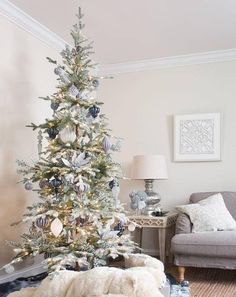 a white christmas tree with blue and silver ornaments in a living room decorated for christmas