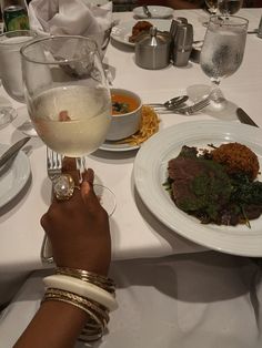 a person holding a wine glass at a table with food and silverware on it