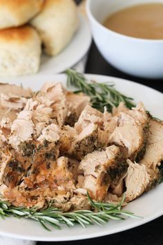 a white plate topped with sliced meat next to bread and a cup of coffee on a table