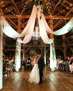 a bride and groom kissing in front of their wedding party at the reception hall with white draping