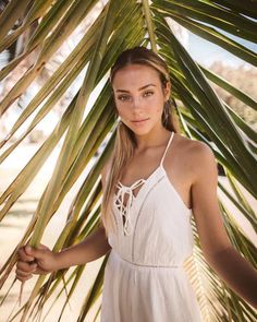 a woman in a white dress standing under a palm tree with her hands on her hips