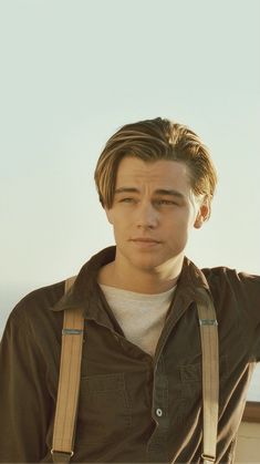 a young man with suspenders and a brown jacket is looking at the camera while standing on top of a hill