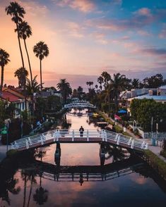 people walking across a bridge over a small river at sunset in the middle of town