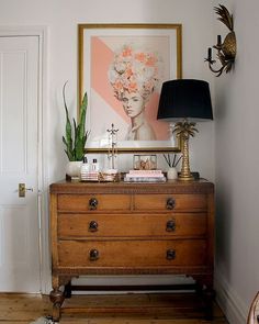 a wooden dresser sitting in front of a painting on the wall next to a lamp