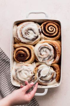 a person holding a spoon in a pan filled with cinnamon rolls