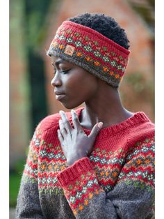 a woman wearing a knitted headband and holding her hands to her chest while looking down