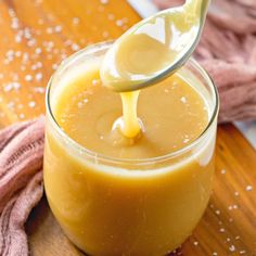 a spoon full of liquid being poured into a glass jar on top of a wooden table