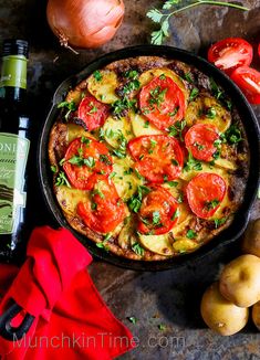 a pizza in a pan with tomatoes, onions and herbs next to some wine bottles