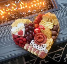 a heart shaped platter filled with fruits and cheeses next to a fire place