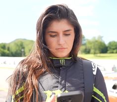 a woman with long hair is looking at her cell phone while standing in front of a race track