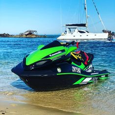 a green and black jet ski is in the water next to a boat on the beach