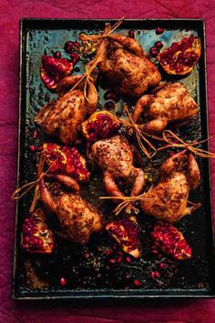 roasted chicken with pomegranates and herbs on a black tray over a red tablecloth