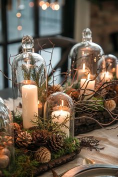 candles are lit in glass domes with pine cones and greenery on the table top