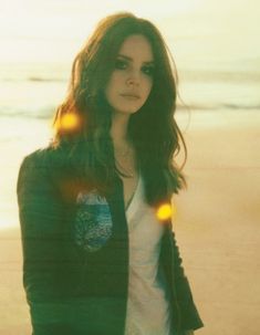 a woman standing on top of a beach next to the ocean with her hands in her pockets