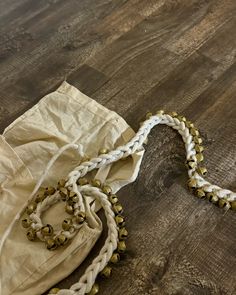 a white and gold beaded necklace laying on top of a wooden floor next to a bag