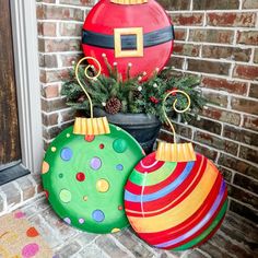 three brightly colored christmas ornaments are sitting on the front door sill next to a potted plant