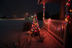 a christmas tree is lit up on the porch in front of a house at night