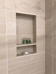 a white tiled bathroom with shelves and soap dispensers on the shelf above