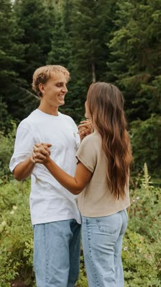 a young man and woman standing next to each other in front of some tall trees