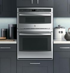 a stainless steel oven and microwave in a kitchen with gray cabinets, white counter tops and blue tile backsplash